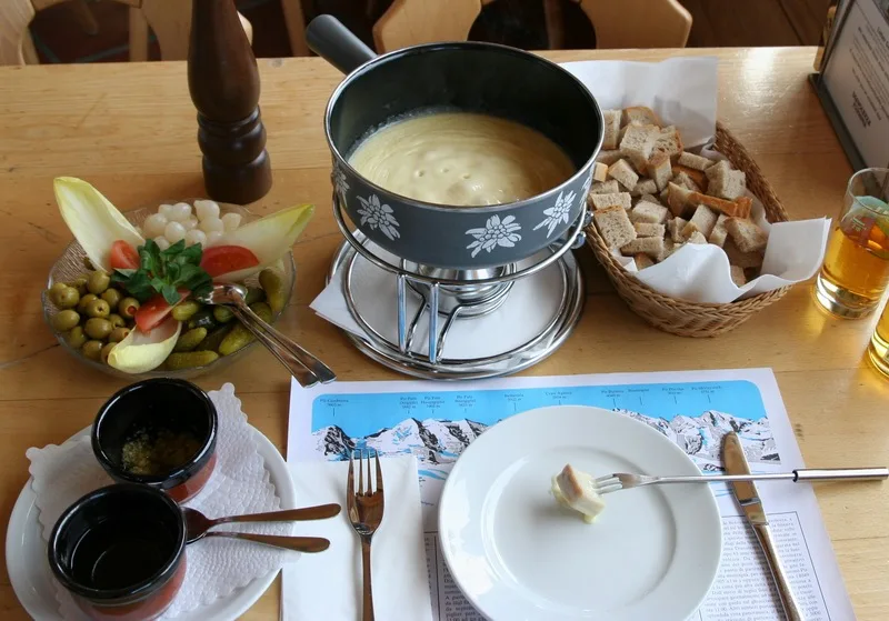 A full Swiss cheese fondue set with bread, pickles, and kirsch